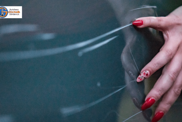 Eine Frauenhand mit rot lackierten Fingernägeln kratzt an einer Autotür entlang und verursacht Kratzer im Lack.